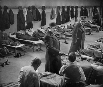 Movie still from “M” (1931), directed by Fritz Lang – A group of men standing in a room with beds; Wide shot, High angle