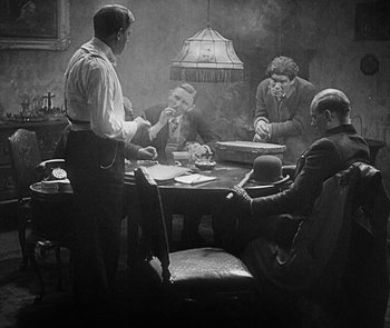 Movie still from “M” (1931), directed by Fritz Lang – A group of men sitting around a table; Medium shot, Over the shoulder angle