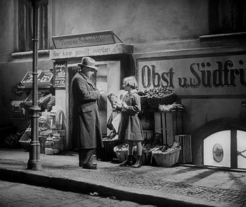 Movie still from “M” (1931), directed by Fritz Lang – A man and a woman standing on the side of the street; Wide shot, High angle