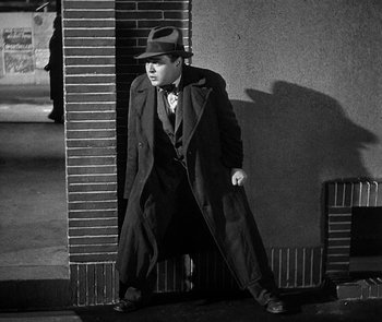 Movie still from “M” (1931), directed by Fritz Lang – A black and white photo of a man leaning against a wall; Wide shot, High angle