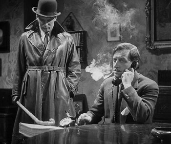 Movie still from “M” (1931), directed by Fritz Lang – A man smoking a cigarette next to another man in a trench coat; Medium shot, Low angle