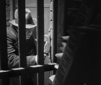 Movie still from “M” (1931), directed by Fritz Lang – A man wearing a hat looking through bars of a jail cell; Medium shot, Low angle