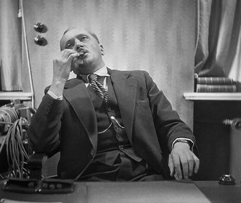 Movie still from “M” (1931), directed by Fritz Lang – A man sitting at a table with a phone in his hand; Medium shot, Low angle