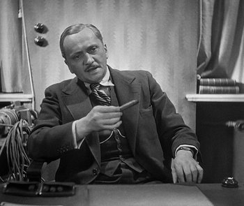 Movie still from “M” (1931), directed by Fritz Lang – A man sitting at a table with a tie around his neck; Medium shot, High angle