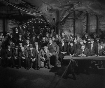 Movie still from “M” (1931), directed by Fritz Lang – A group of men sitting around a table in front of a brick wall; Wide shot, High angle