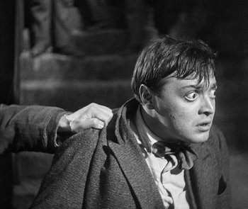 Movie still from “M” (1931), directed by Fritz Lang – A black - and - white photo of a man holding a jacket over his shoulder; Close Up shot, Over the shoulder angle