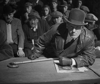 Movie still from “M” (1931), directed by Fritz Lang – An old photo of a man writing on a piece of paper; Medium shot, High angle