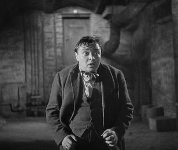 Movie still from “M” (1931), directed by Fritz Lang – A man standing in a dark room with his hands in his pockets; Medium shot, High angle