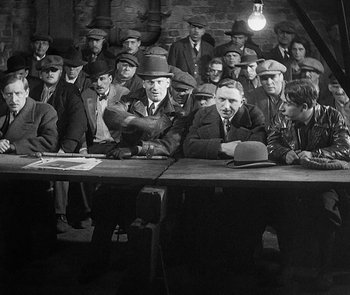 Movie still from “M” (1931), directed by Fritz Lang – A group of men sitting at a table in front of a light; Medium shot, High angle