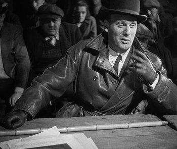 Movie still from “M” (1931), directed by Fritz Lang – An old photo of a man sitting at a table in front of other men; Medium shot, Over the shoulder angle