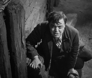 Movie still from “M” (1931), directed by Fritz Lang – A black and white photo of a man leaning against a wall; Medium shot, High angle