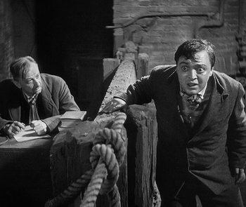 Movie still from “M” (1931), directed by Fritz Lang – A man standing next to another man with a rope; Medium shot, High angle