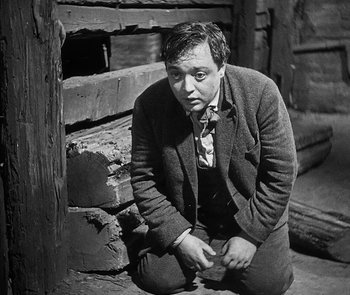 Movie still from “M” (1931), directed by Fritz Lang – A man kneeling on the ground in front of a brick wall; Medium shot, High angle