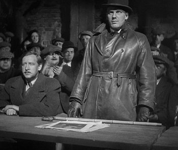 Movie still from “M” (1931), directed by Fritz Lang – An old photo of a man standing in front of a crowd; Medium shot, Over the shoulder angle