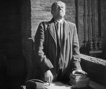 Movie still from “M” (1931), directed by Fritz Lang – An older man standing at a table with a stack of books; Medium shot, Low angle