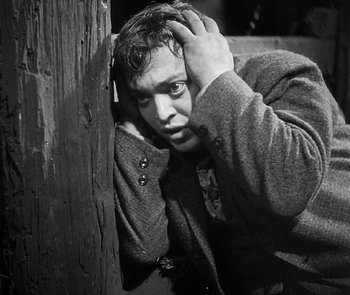 Movie still from “M” (1931), directed by Fritz Lang – A black and white photo of a man leaning against a wooden post; Close Up shot, High angle