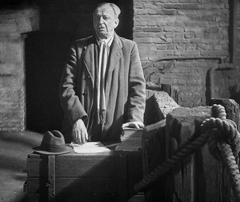 Movie still from “M” (1931), directed by Fritz Lang – An older man standing next to a trunk; Medium shot, High angle