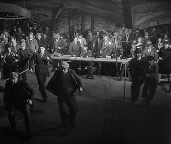 Movie still from “M” (1931), directed by Fritz Lang – A black and white photo of a group of men in suits; Wide shot, High angle