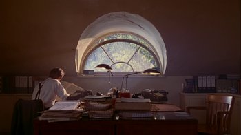 Movie still from “M. Butterfly” (1993), directed by David Cronenberg – A woman sitting at a desk in front of an open window; Wide shot, Low angle