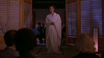 Movie still from “M. Butterfly” (1993), directed by David Cronenberg – A woman in a white robe standing in front of a group of people; Medium shot, Over the shoulder angle