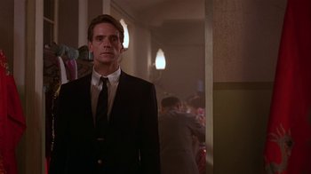 Movie still from “M. Butterfly” (1993), directed by David Cronenberg – A man wearing a suit and tie standing in a hallway; Medium shot, Low angle