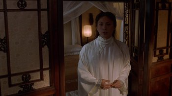 Movie still from “M. Butterfly” (1993), directed by David Cronenberg – A woman standing in front of an open door in a room; Medium shot, High angle