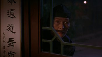 Movie still from “M. Butterfly” (1993), directed by David Cronenberg – An older woman looking out of a window at night; Medium shot, Over the shoulder angle