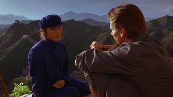 Movie still from “M. Butterfly” (1993), directed by David Cronenberg – A man and a woman sitting on the ground in front of a mountain range; Medium shot, Over the shoulder angle