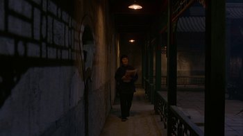 Movie still from “M. Butterfly” (1993), directed by David Cronenberg – A person walking down a dark hallway holding a book; Wide shot, High angle