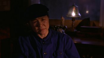 Movie still from “M. Butterfly” (1993), directed by David Cronenberg – An older asian woman wearing a hat and a blue shirt; Close Up shot, Over the shoulder angle