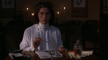 Movie still from “M. Butterfly” (1993), directed by David Cronenberg – A woman sitting at a table painting a picture; Medium shot, Low angle
