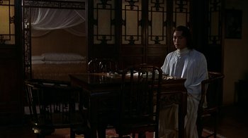 Movie still from “M. Butterfly” (1993), directed by David Cronenberg – A man sitting at a table in front of a bed; Wide shot, High angle