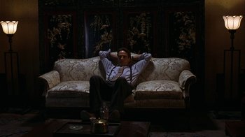 Movie still from “M. Butterfly” (1993), directed by David Cronenberg – A man sitting on top of a couch in a living room; Wide shot, High angle