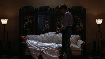 Movie still from “M. Butterfly” (1993), directed by David Cronenberg – A man standing next to a woman laying on a couch; Wide shot, Overhead angle