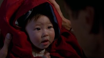 Movie still from “M. Butterfly” (1993), directed by David Cronenberg – A baby wearing a red coat and a blue hat; Close Up shot, High angle