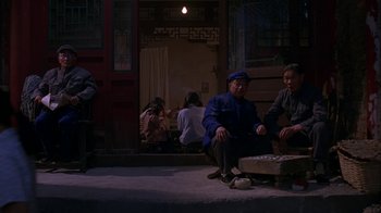 Movie still from “M. Butterfly” (1993), directed by David Cronenberg – A group of people sitting on the ground in front of a building; Wide shot, High angle