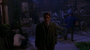 Movie still from “M. Butterfly” (1993), directed by David Cronenberg – A man in a suit and tie standing next to a building; Wide shot, Over the shoulder angle