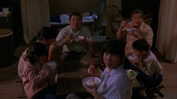 Movie still from “M. Butterfly” (1993), directed by David Cronenberg – A group of people sitting around eating food; Wide shot, High angle