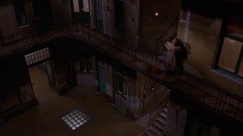 Movie still from “M. Butterfly” (1993), directed by David Cronenberg – Two people standing on the stairs of an old building at night; Extreme Wide shot, Overhead angle