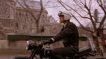 Movie still from “M. Butterfly” (1993), directed by David Cronenberg – A man riding a motorcycle on the street; Medium shot, Low angle