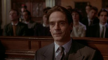 Movie still from “M. Butterfly” (1993), directed by David Cronenberg – A man in a suit sitting in front of a group of people; Close Up shot, Low angle