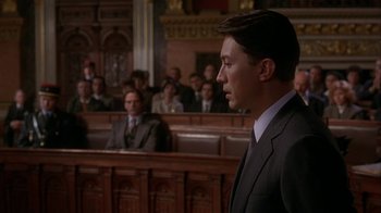 Movie still from “M. Butterfly” (1993), directed by David Cronenberg – A man standing in front of a crowd in a courtroom; Medium shot, Low angle