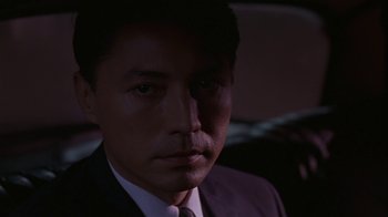 Movie still from “M. Butterfly” (1993), directed by David Cronenberg – A person wearing a suit and tie; Close Up shot, Low angle
