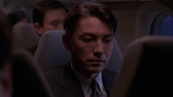 Movie still from “M. Butterfly” (1993), directed by David Cronenberg – A man wearing a suit and tie sitting in a chair; Close Up shot, High angle