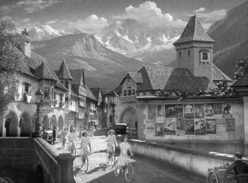 Movie still from “Mad About Music” (1938), directed by Norman Taurog – A black and white photo of people riding bikes in a town; Extreme Wide shot, High angle