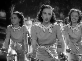 Movie still from “Mad About Music” (1938), directed by Norman Taurog – A group of young women riding bicycles in a parade; Medium shot, Low angle