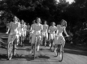 Movie still from “Mad About Music” (1938), directed by Norman Taurog – A black and white photo of a group of women riding bikes; Wide shot, High angle
