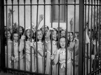 Movie still from “Mad About Music” (1938), directed by Norman Taurog – A group of young girls standing next to each other behind a fence; Wide shot, High angle