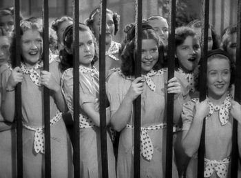 Movie still from “Mad About Music” (1938), directed by Norman Taurog – A group of young girls standing next to each other behind bars; Medium shot, High angle