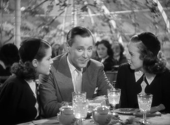 Movie still from “Mad About Music” (1938), directed by Norman Taurog – A man and two girls sitting at a table under an umbrella; Medium shot, Over the shoulder angle